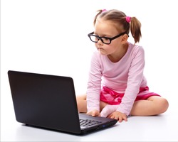 Cute little girl is sitting on floor with her laptop, wearing glasses, isolated over white