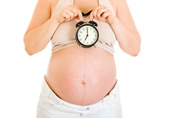 Pregnant woman holding alarm clock near her tummy isolated on white. Close-up.