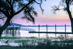 Pinkish purple Sunset at Bloody Pointe on Daufuskie Island, SC at a pier on a desolate island off the coast of South Carolina. Silhouette trees in foreground and a dock/ Daufuskie September sunset