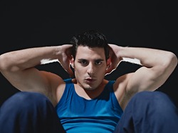 young adult caucasian male in blue sportswear exercising abdominals on black background, looking at camera. Horizontal shape, front view, copy space