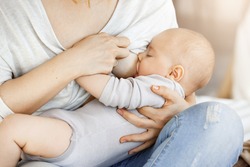 Close up of young mother who breastfeed her little kid. Touching scene of maternity love and caring. Family, motherhood and lifestyle concept.