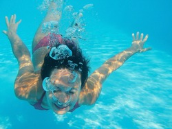 Woman swimming underwater in pool smiling. Young female swimmer at holiday resort.