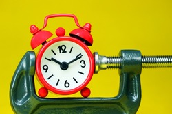 A red alarm clock placed in a Grey clamp against a pastel yellow background, asking the question do you manage your time effectively?