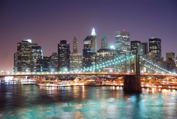 New York City Brooklyn Bridge and Manhattan skyline with skyscrapers over Hudson River illuminated with lights at dusk after sunset.