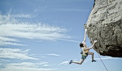 Female rock climber struggles to reach her next grip as she battles her way up a steep cliff in Joshua Tree National Park, California.