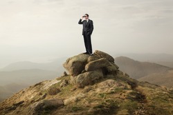 Businessman using binoculars on a rock in the mountains