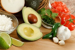 Fresh avocado surrounded by onion, tomato, garlic, jalepeno peppers and lime, ready for preparing guacamole