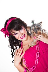 Portrait of beautiful girl with dark long curly hair and vibrant make-up wearing pink satiny ribbon holding small dog on white background
