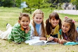 Portrait of cute kids lying on lawn and looking at camera with open book near by