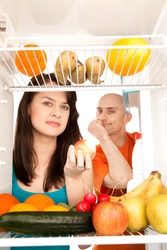 Young couple eating and looking at healthy fruit and vegetable in modern refrigerator, isolated on white background.