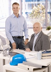 Portrait of senior and junior businessmen working in office, looking at camera, smiling.?