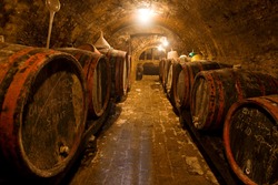 Wine barrels and bottles in the back in a cellar . Warm colors, wide angle view.