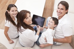 An attractive happy, family of mother, father, son and daughter sitting on a sofa at home having fun using a tablet computer