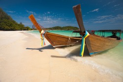 Two traditional longtail boats parked on a white sand beach surrounded by crystal clear turquoise water on a sunny, blue sky day on the Thai paradise island of Ko Lipe, Thailand. Horizontal copy space