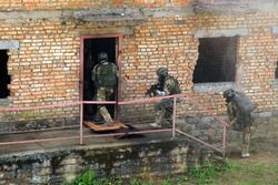 Special forces soldier during a black tactical exercises. Army Soldier in full tactical gear with weapons and gas mask. Intrusion inside the building after the detonation of an explosive.