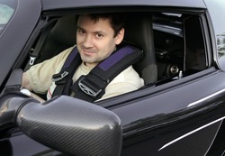 Young man, racer sitting in sport black car and looking from opened window with smiling