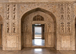 Decorated marble wall frames gate and door at Agra Fort Palace in India. Alcoves and yellow red green in-lay marble work of royal chambers, Taj Mahal in the far distance.