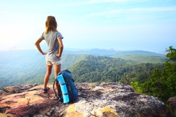 Young woman standing with backpack on cliff's edge and looking into a wide valley