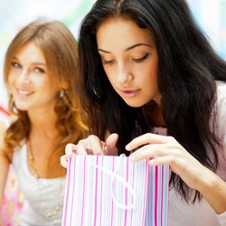 Two excited shopping woman resting on bench at shopping mall. Looking into shopping bags