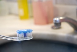 Detail shot of a tooth brush with tooth paste on it and basin in the blurred background