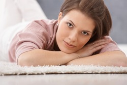 Portrait of attractive young woman lying on floor carpet, smiling at camera.?