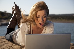 A woman in the outdoors working on her computer with a shocked expression on her face.