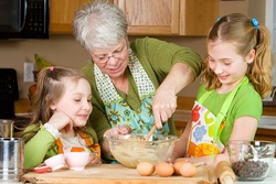 Happy Family featuring a friendly Grandma baking cookies in a home kitchen with her two Grandchildren.