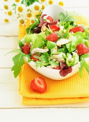 Green salad with strawberry, chicken, nuts, cheese in a white bowl on the table