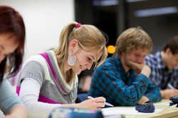 pretty, female college student sitting in a classroom full of students during class (shallow DOF; color toned image)