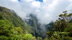 Scenic view of Trou de fer waterfall on Reunion Island National Park with cloudscape background and jungle in foreground.
