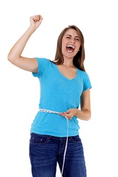 pretty young woman rejoicing over weight loss success. One hand holds a tape measure, the other is raised in triumph as she shouts for joy at her accomplishment