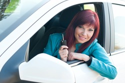 Smiling caucasian red-haired young woman sitting in a car and demonstrating the keys