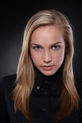 Studio portrait of unsmiling, blonde teenager in black, black background .?