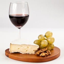 Piece of Brie french cheese with grapes and nuts over an hearth shaped wooden board and a glass of red wine in isolated studio shot