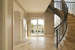 Staircase and front door area of a modern house. Staircase is framed on the right and the outside is visible through the front door. Both the staircase and floor is tiled
