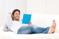 Smiling relaxed man reading a book lying on sofa
