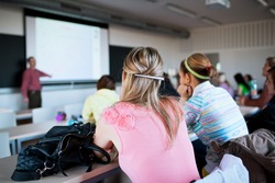young, pretty female college student sitting in a classroom full of students during class (shallow DOF; color toned image)