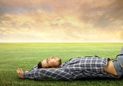 Handsome young man relaxing on a green meadow