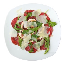 white dish with carpaccio of beef on arugula over white background. Top view.