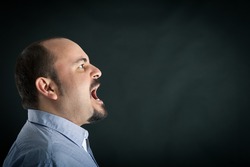 Angry man shouting against black background with room for your text. Conceptual image.
