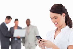 Businesswoman writing text message with colleagues behind her against a white background