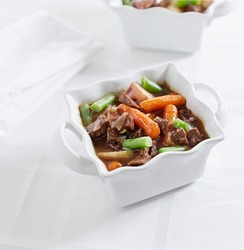 beef stew with potatoes, carrots, and green beans on a white tablecloth with copyspace
