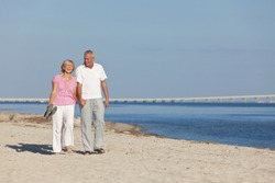 Happy senior man and woman couple together holding hands and walking on a deserted tropical beach