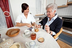 a geriatric nurse helps elderly woman at breakfast