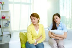Photo of offended woman sitting on sofa with her teenage daughter being sorry for what she did