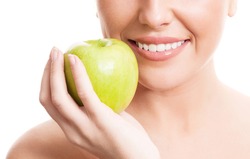 closeup of the face, hands and healthy white teeth of a woman holding an apple, isolated against white background