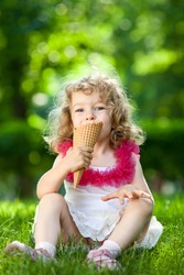 Beautiful child eating ice-cream outdoors in spring park against natural green background