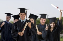 Young man wearing graduation cap and gown with classmates