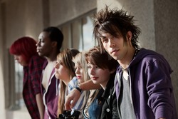 Young punk boy looks at the camera as his friends look away into the distance.