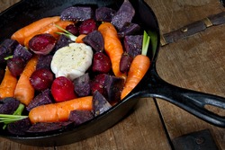 Raw root vegetables in a cast iron skillet ready for the oven. Vegetables include carrots, red beets, garlic and purple potatoes.